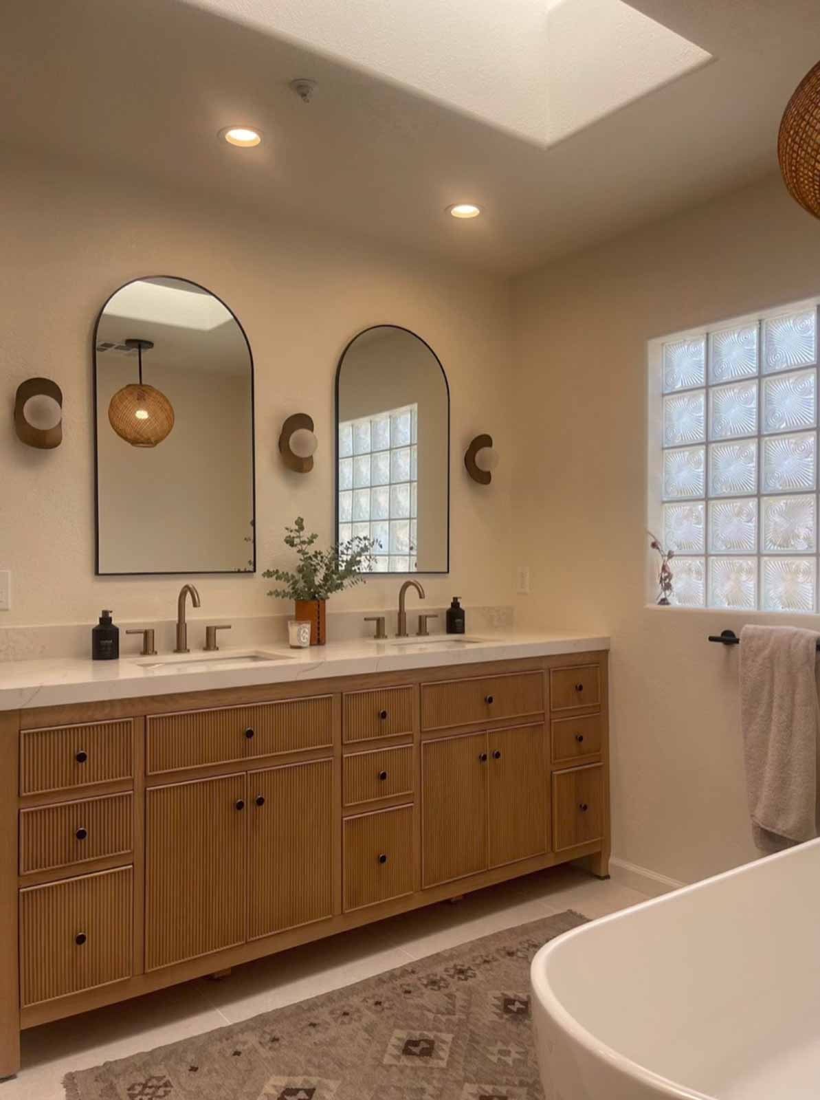 Double vanity with oak cabinets, dual arch mirrors, and brass wall sconces in Glendale