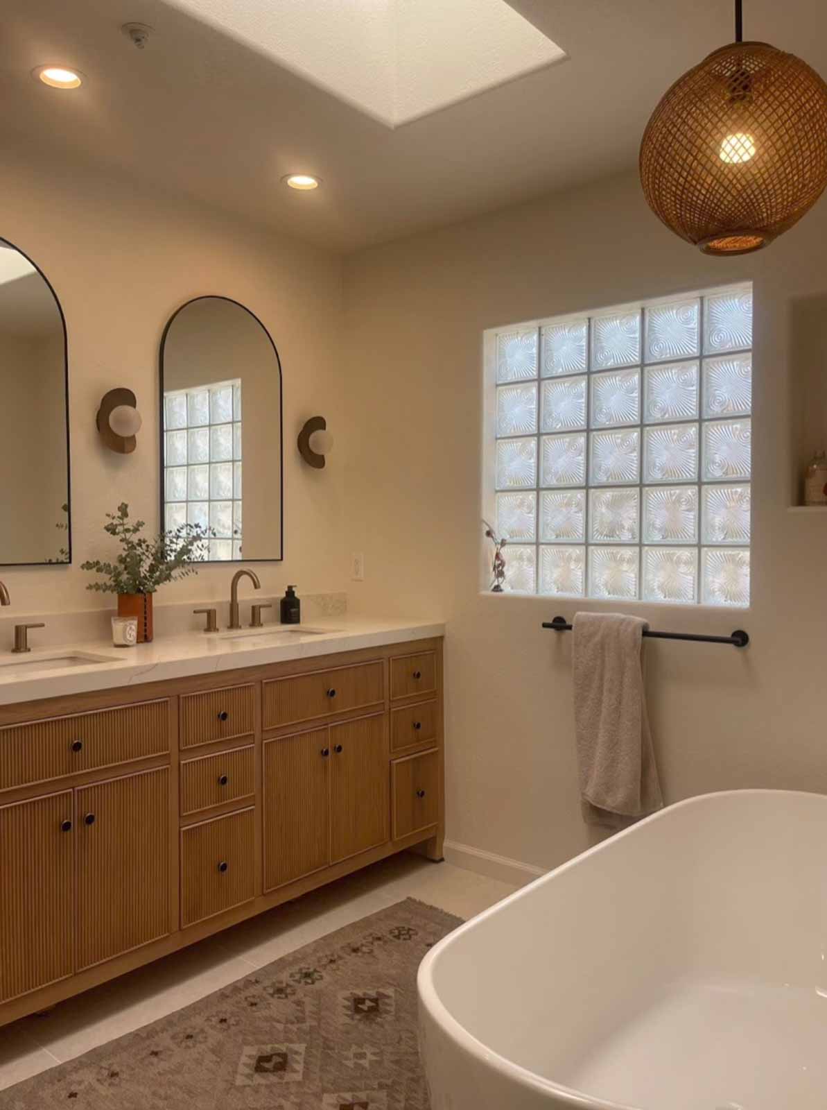 Natural light bathroom with dual mirrors, glass block window, and freestanding tub in Glendale