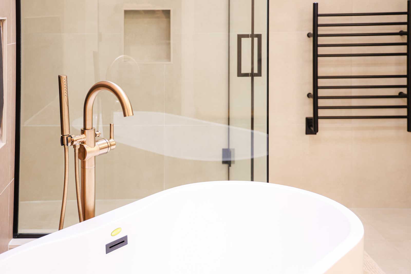 Elegant freestanding white soaking tub with rose gold floor-mounted faucet and glass shower enclosure - spa bathroom renovation LA County