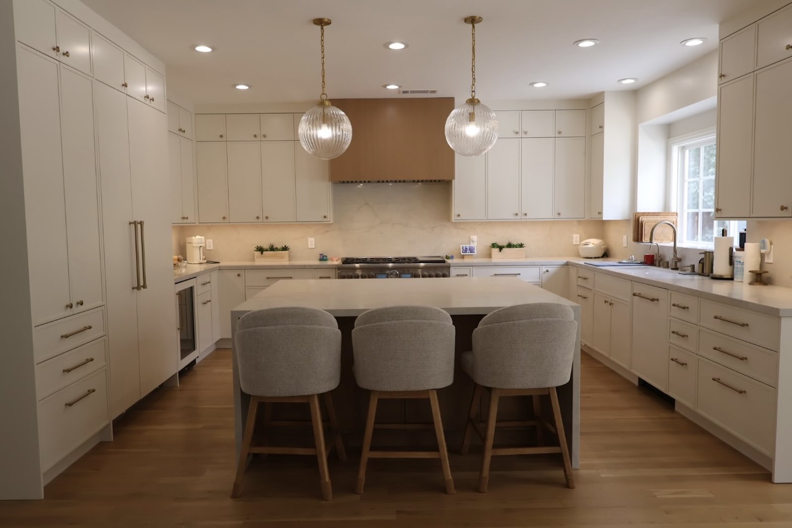 La Cañada Flintridge kitchen island with upholstered stools, globe pendants, and cream cabinetry